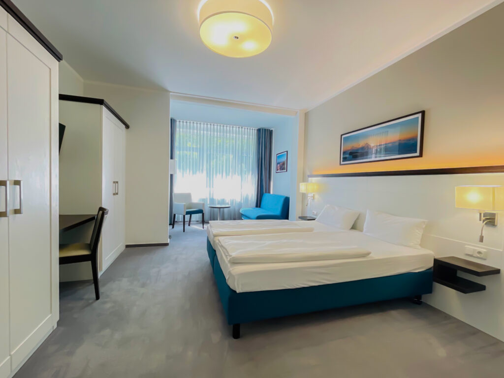 Moderne Hotelzimmer mit zwei Einzelbetten, Schreibtisch und Fenster mit Tageslicht.